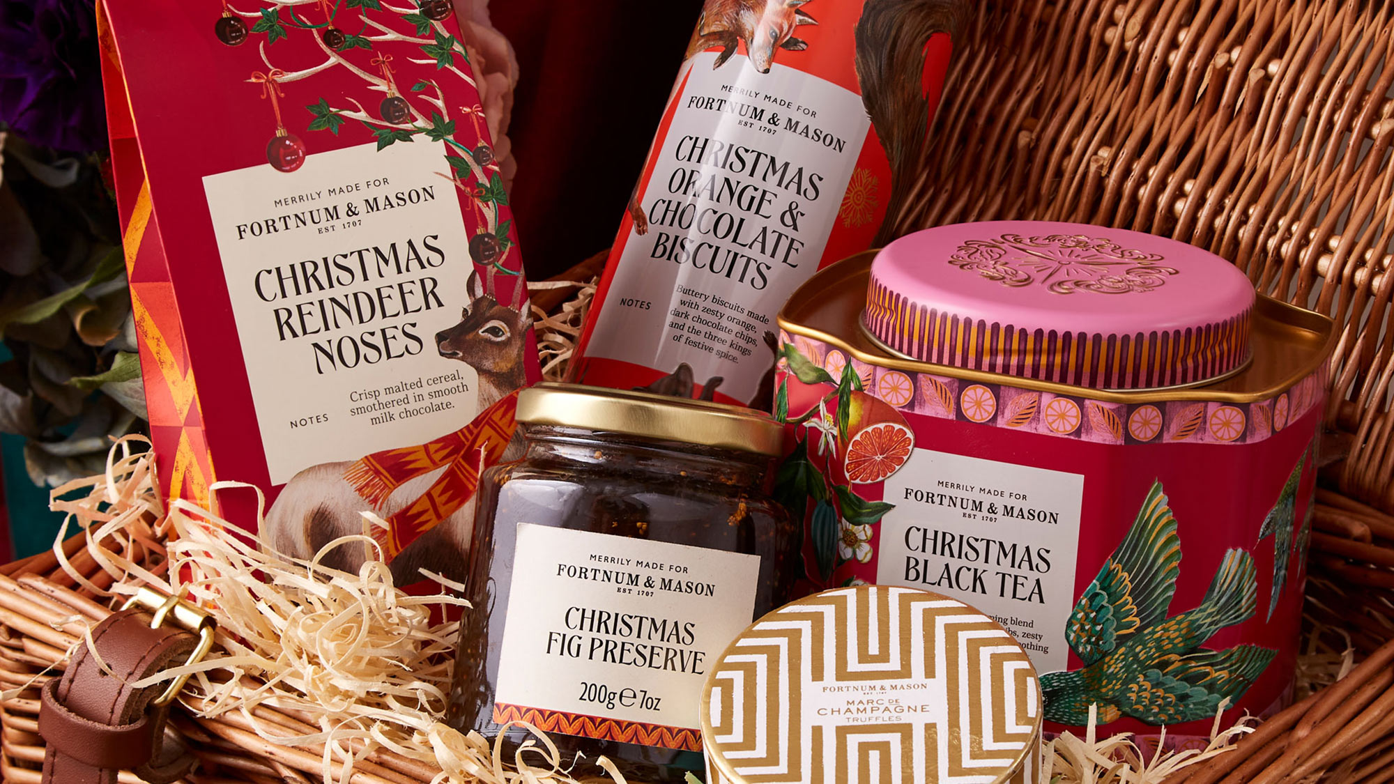 A wicker hamper filled with Christmas-themed Fortnum & Mason products, including tea, preserves, and confectionery.