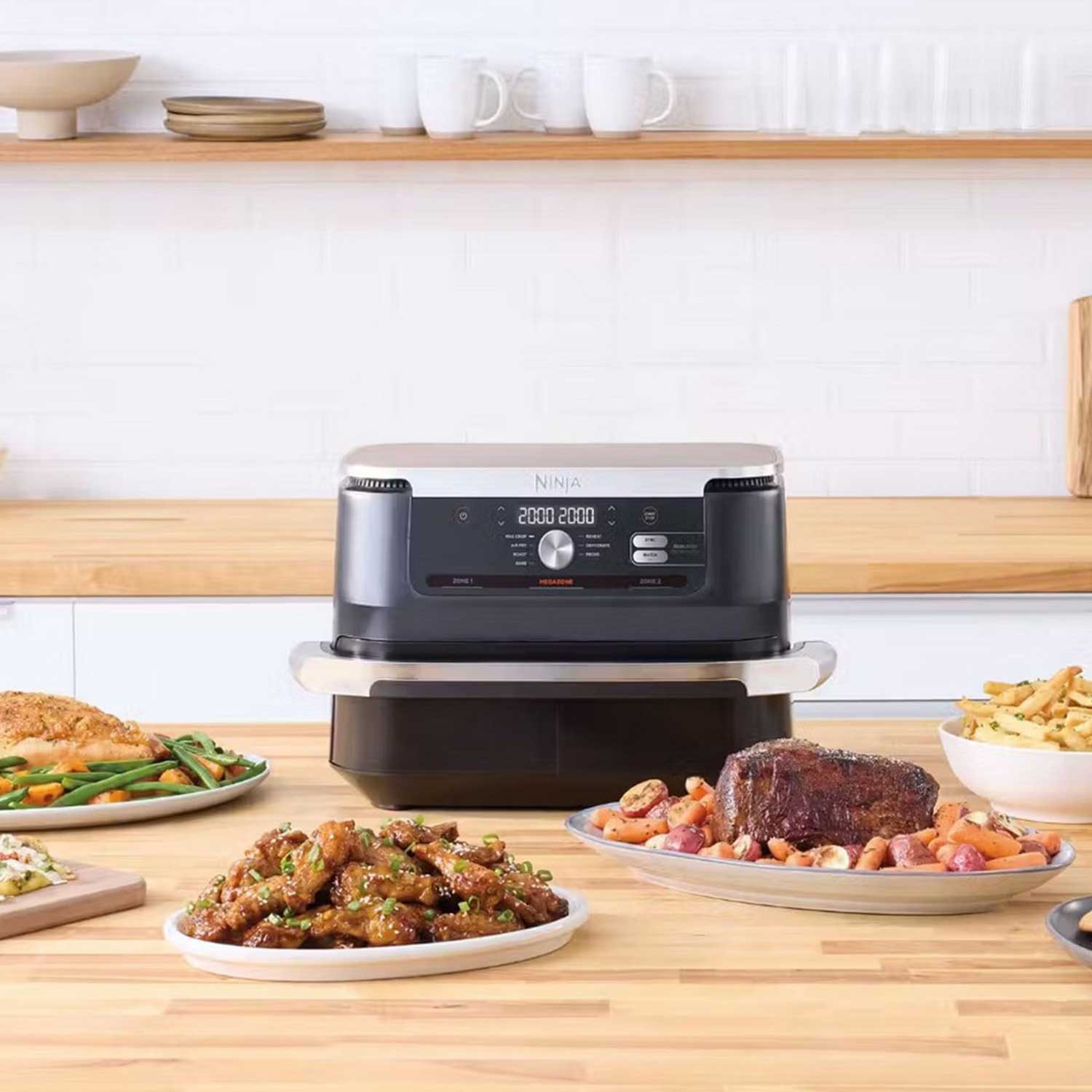 A countertop grill with cooked dishes, including roasted vegetables, meat, and fries, on a wooden kitchen counter.