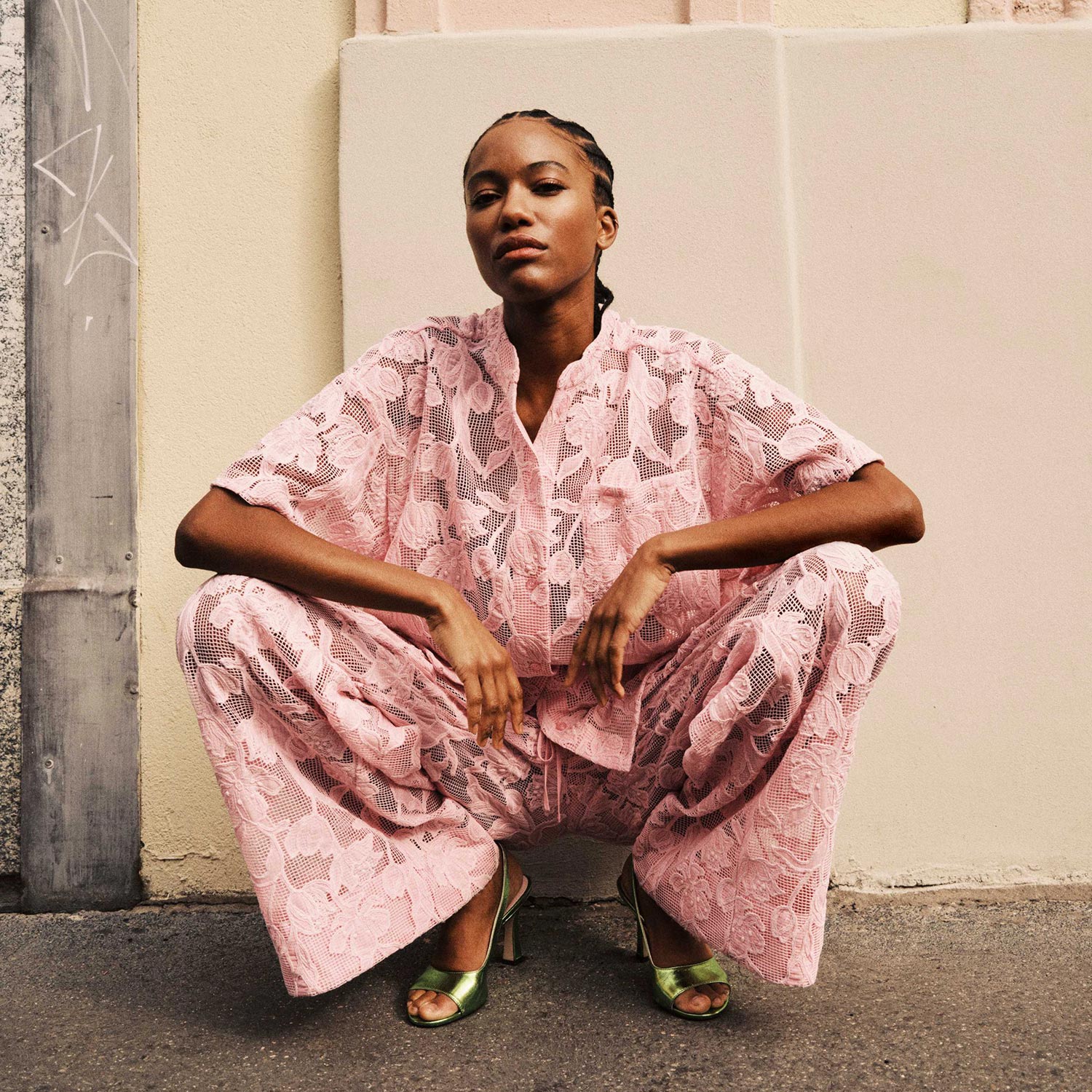 Person squatting in a pink floral outfit against a building background.