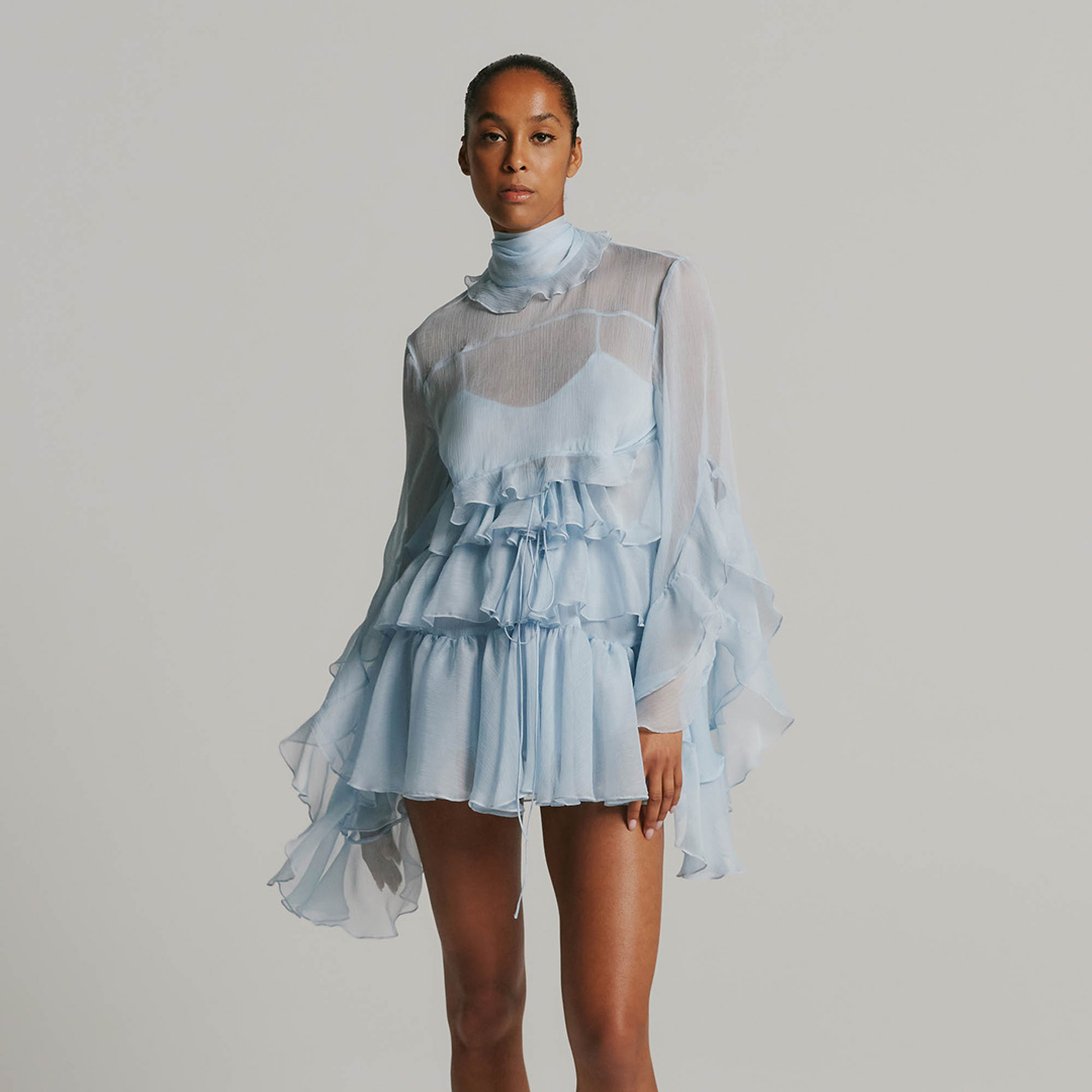 Model wearing a light blue, sheer ruffled dress and beige platform heels.