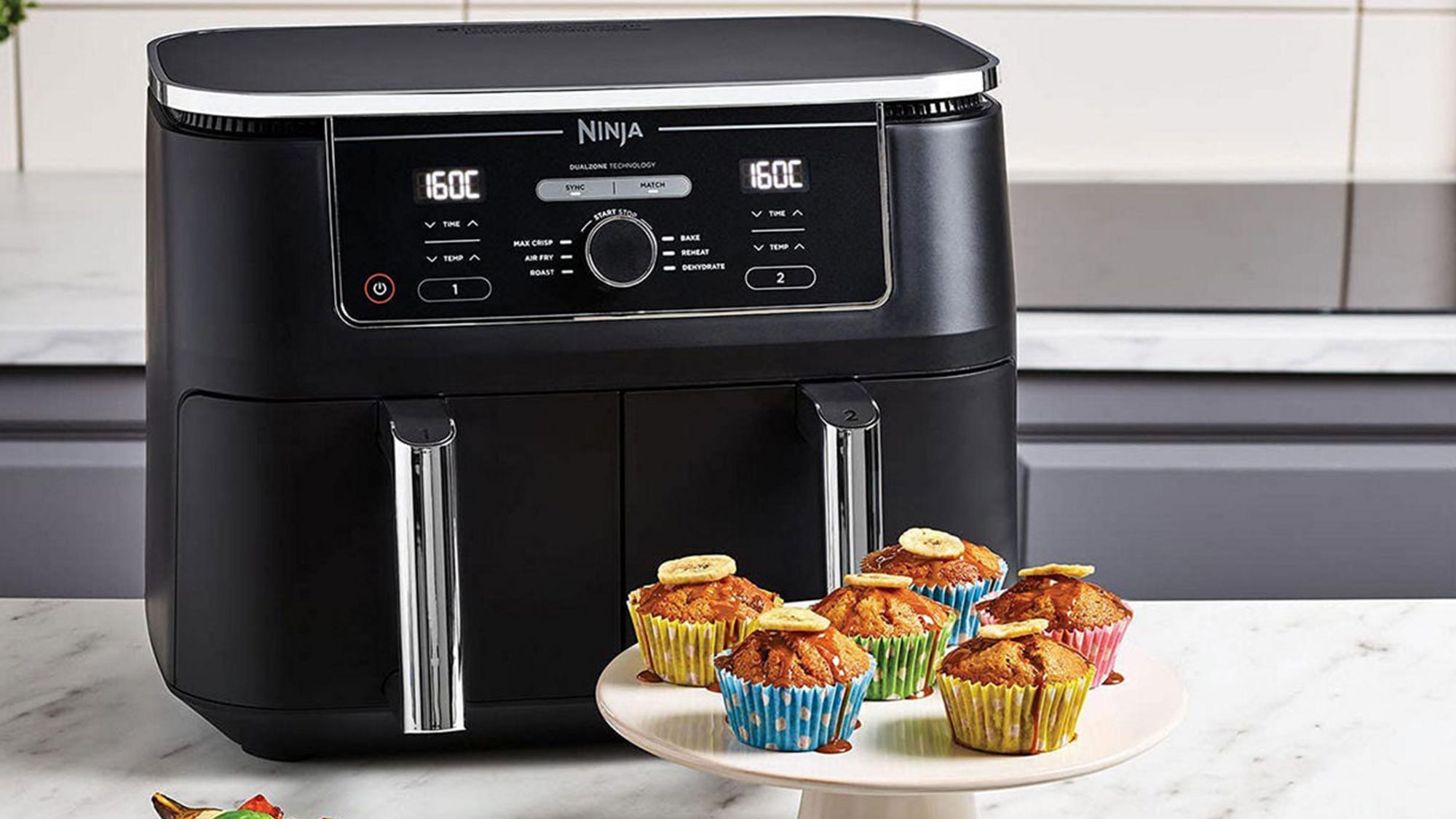 Black Ninja air fryer with dual zone technology displaying cooked muffins on a plate in front