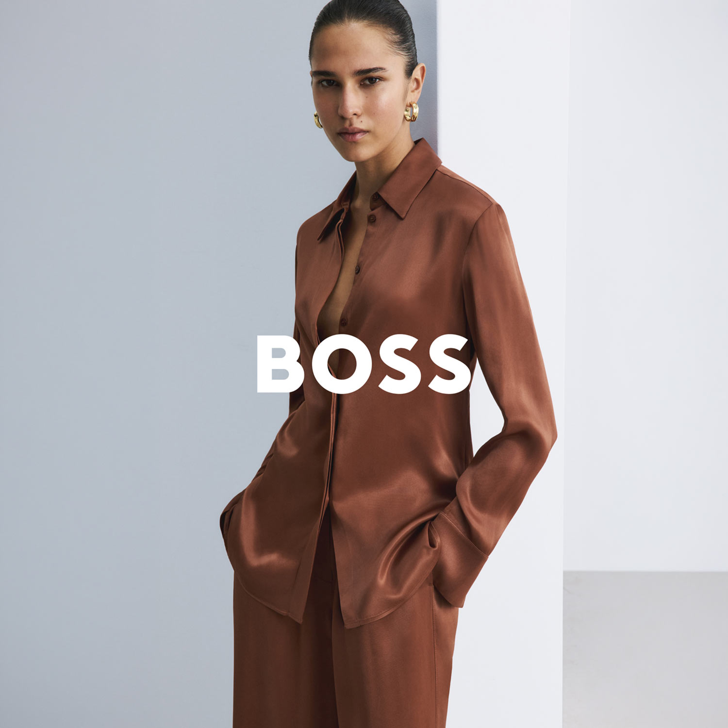 Woman wearing rust-coloured silk shirt and matching tailored trousers against neutral backdrop