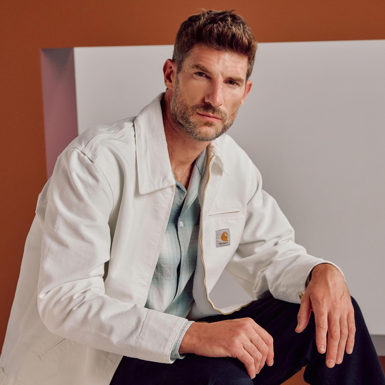 Man wearing cream Carhartt jacket over blue shirt against brown and grey background