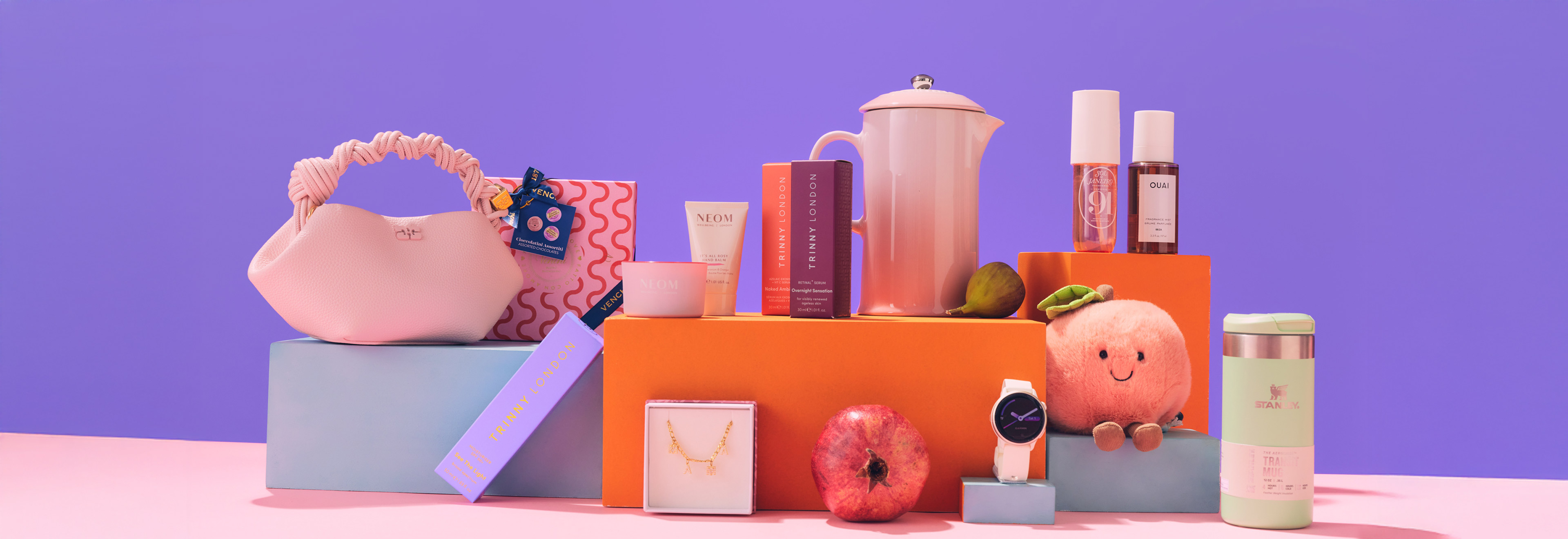 A colorful arrangement of various items including a purse, skincare products, jewelry, a smartwatch, and a cute plush toy on pastel blocks.