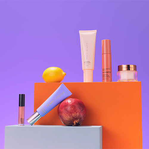 Cosmetic products and fruits displayed on colorful blocks against a purple background.