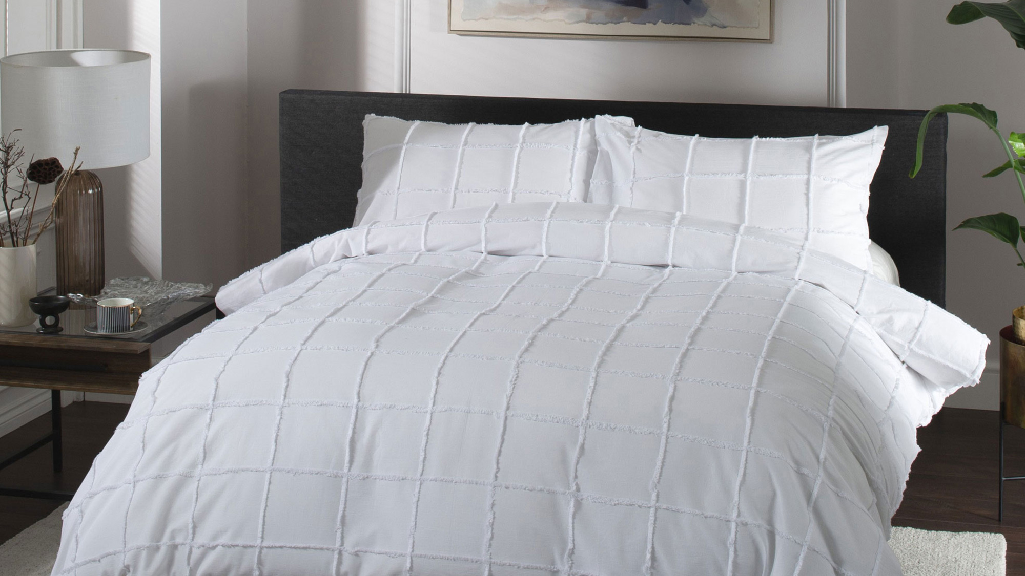 Bedroom styled with white quilted duvet set on dark headboard bed, side table with lamp and accessories