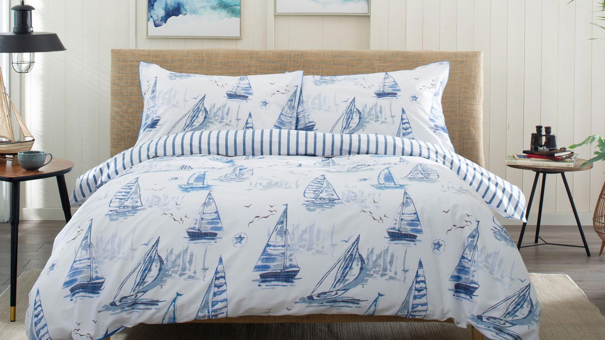 Bedroom with blue and white nautical patterned duvet set, striped cushions, and coastal décor styling