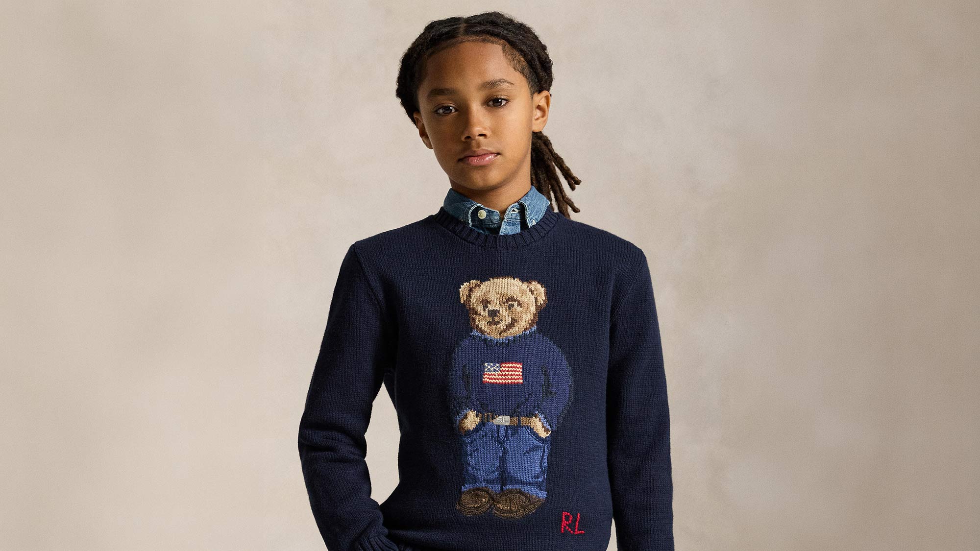 Child wearing navy knit jumper with embroidered bear design wearing blue jumper with flag motif