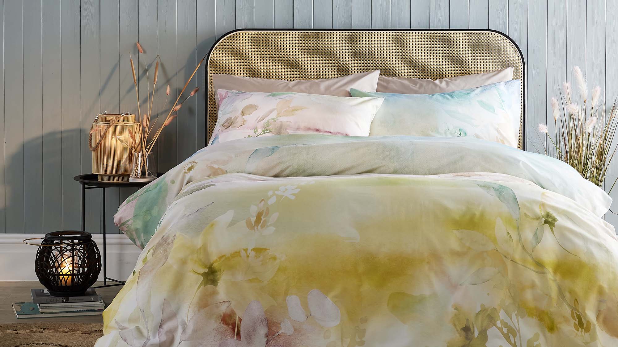 Bedroom styled with floral duvet set on rattan headboard bed, woven basket with dried flowers, and decorative black lantern