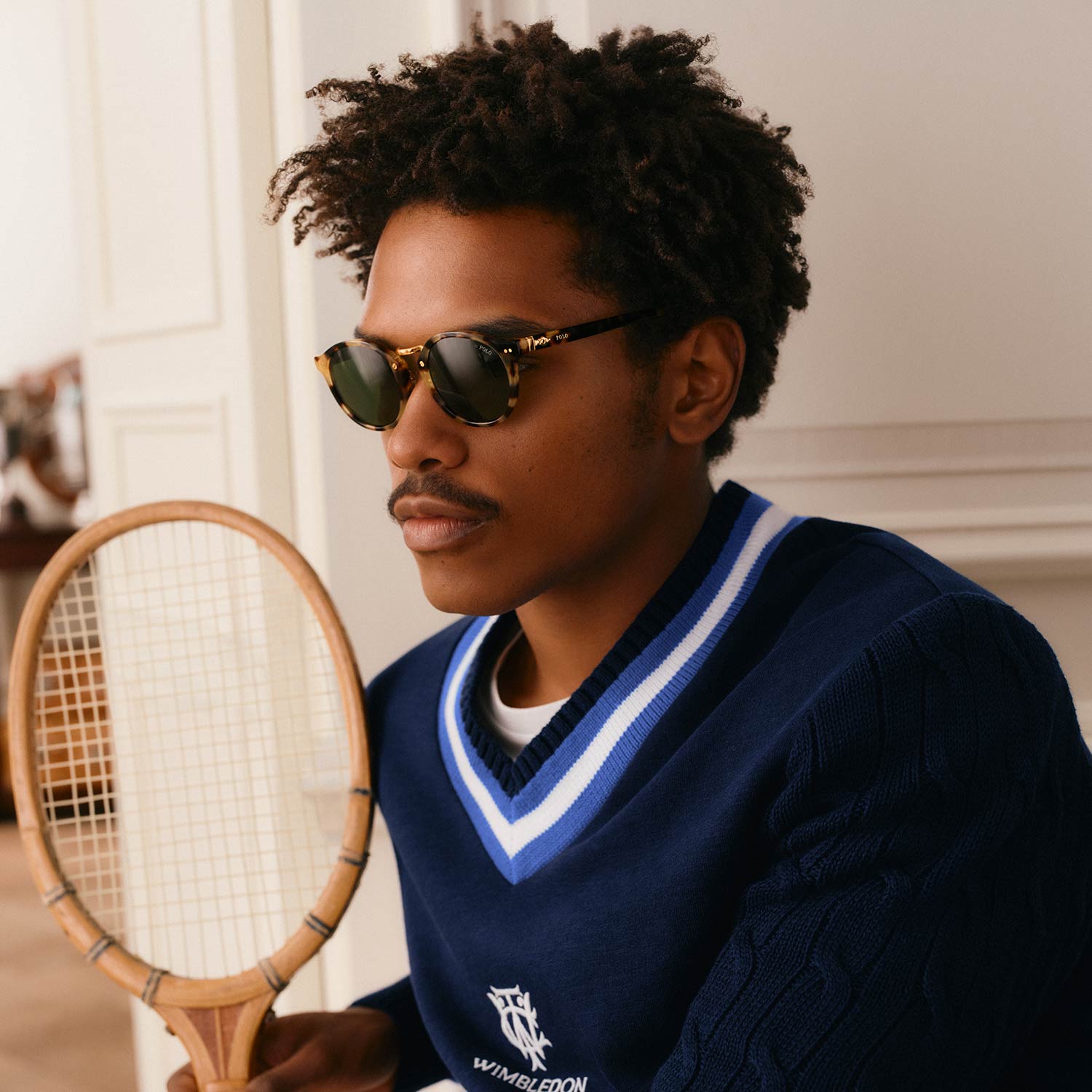 Man wearing navy Polo Ralph Lauren V-neck knit with blue and white stripes, holding tennis racket