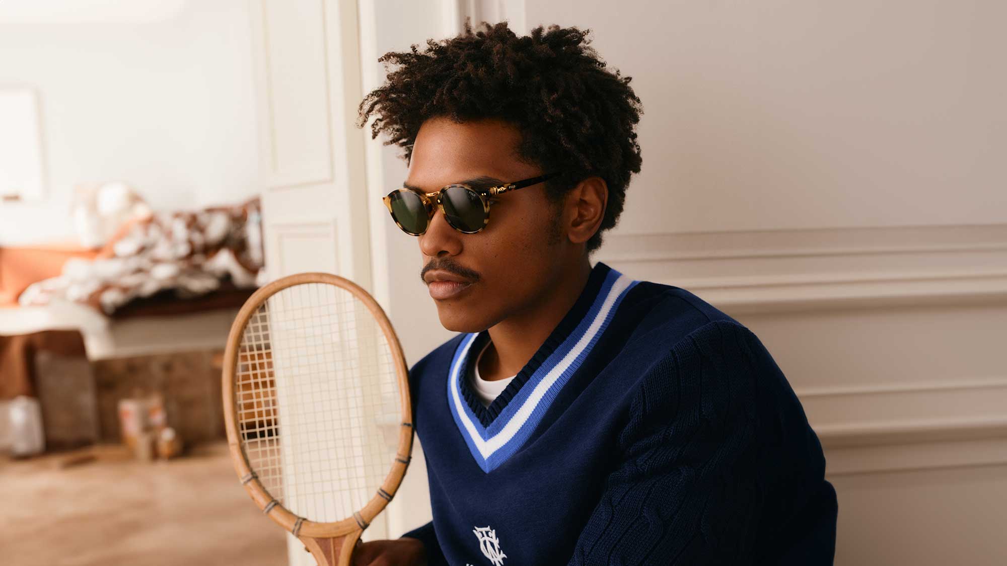 Man wearing navy Polo Ralph Lauren V-neck knit with blue and white stripes, holding tennis racket