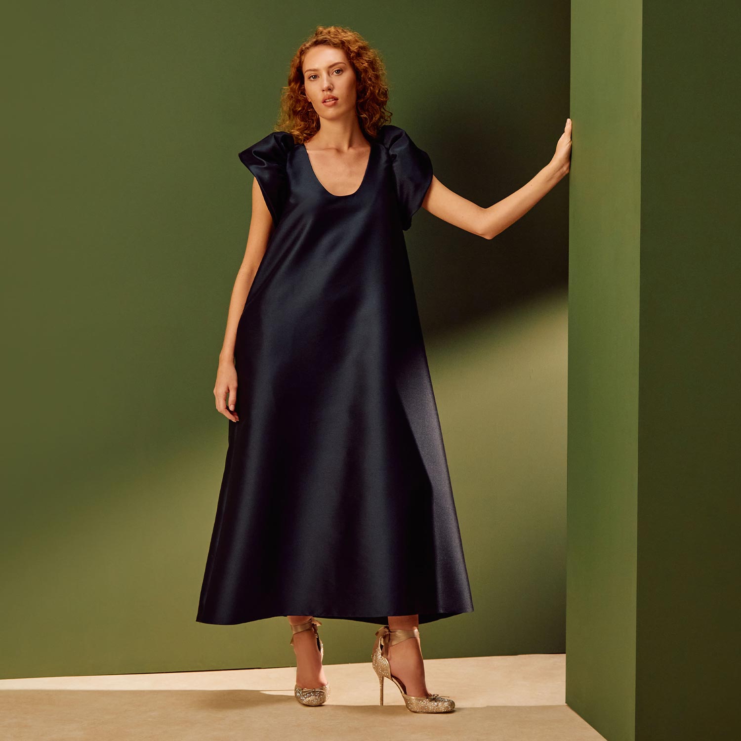 Woman wearing navy A-line midi dress with cap sleeves and metallic heels against green and beige backdrop