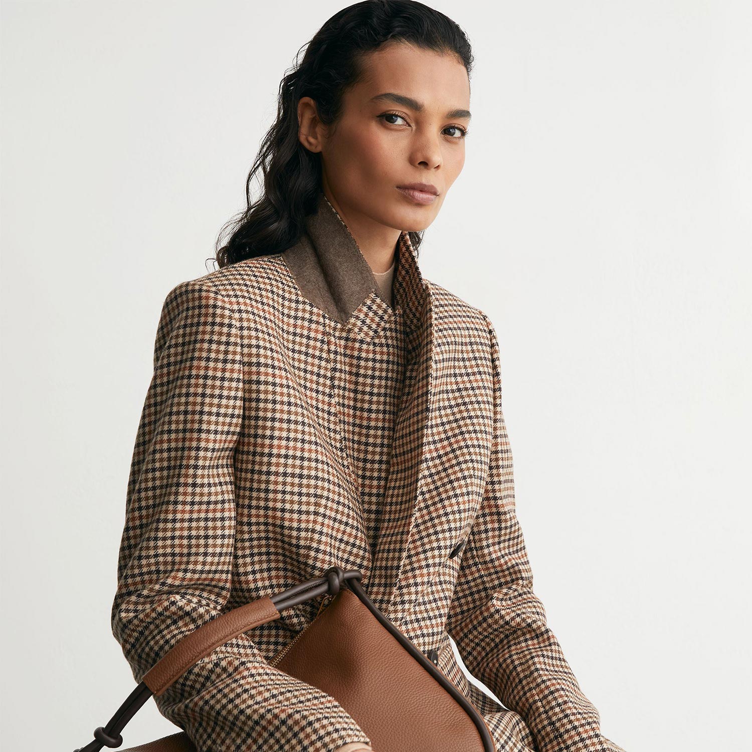 Woman wearing brown houndstooth blazer and matching trousers, holding a tan leather handbag