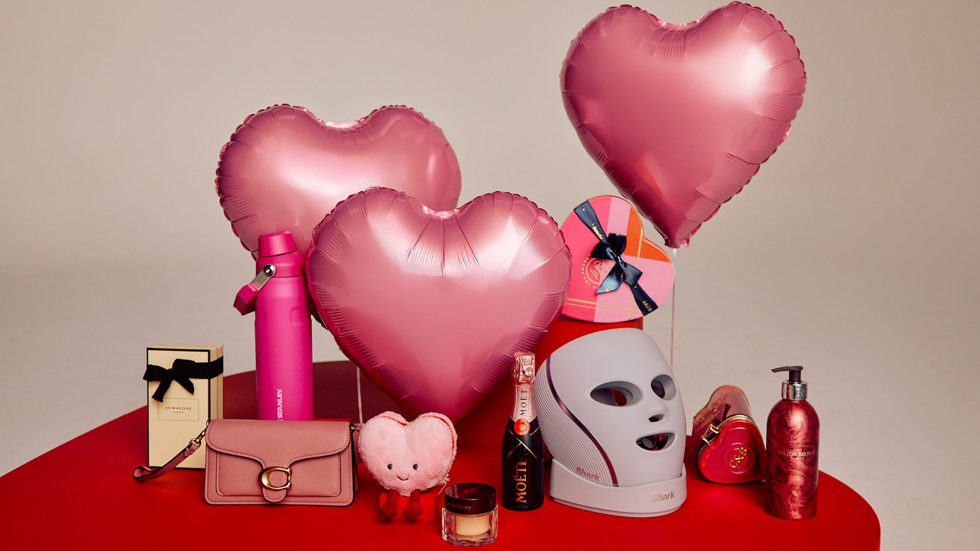 A display of heart-shaped balloons, beauty products, and accessories on a red table.