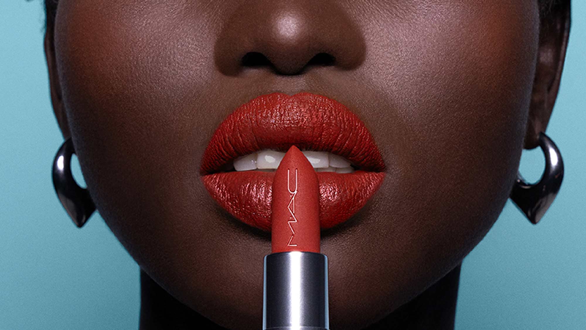 Close-up of a person with glossy red lips holding a red M.A.C lipstick.