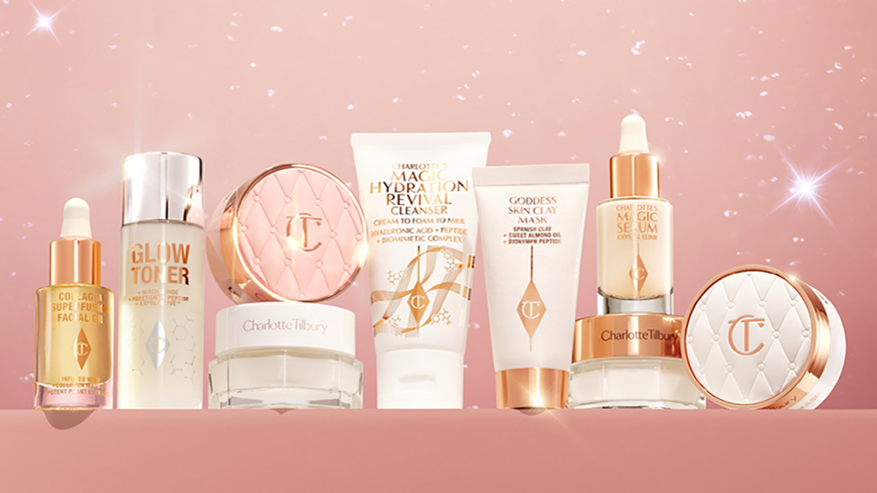 A collection of skincare and cosmetic products displayed against a sparkling pink background.