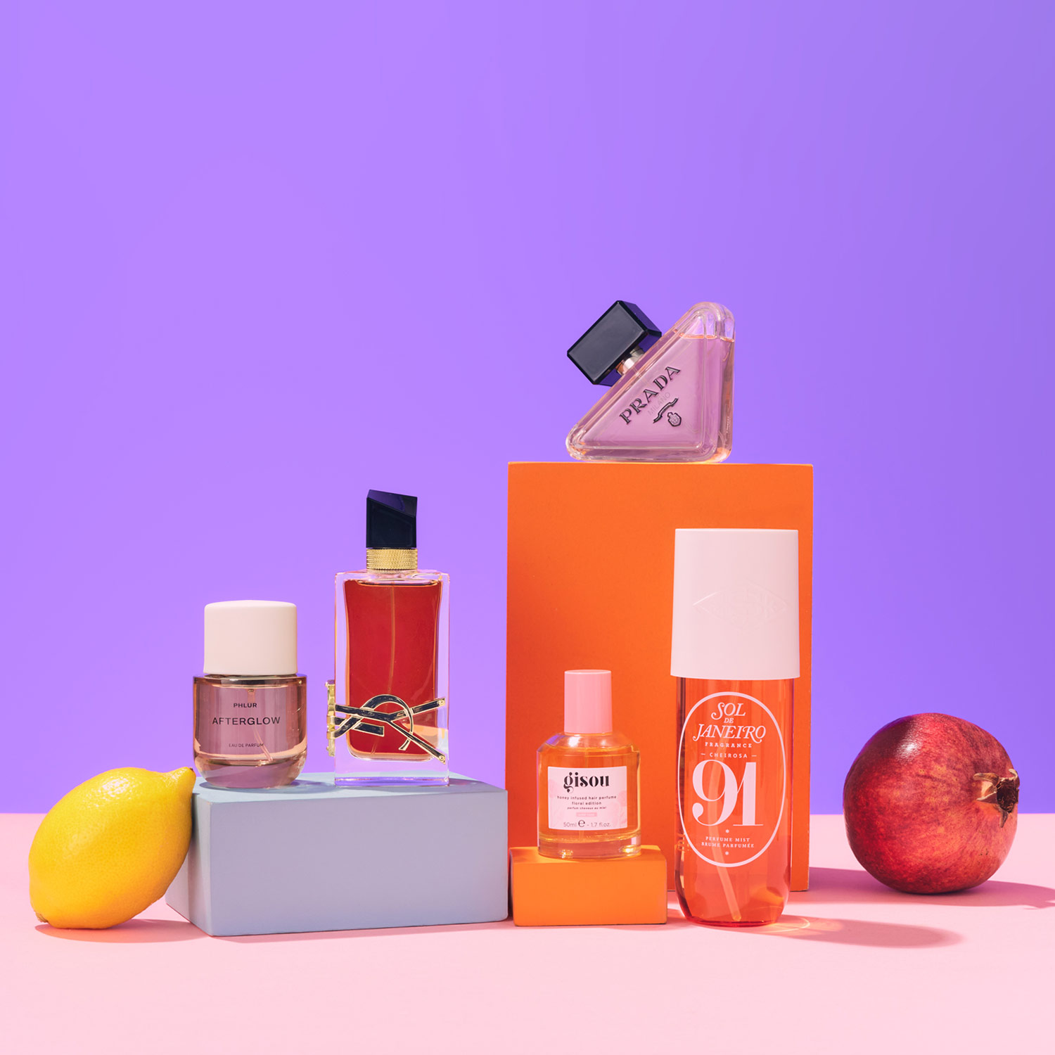 Perfume bottles displayed on colorful boxes with a lemon and an apple, set against a purple background.