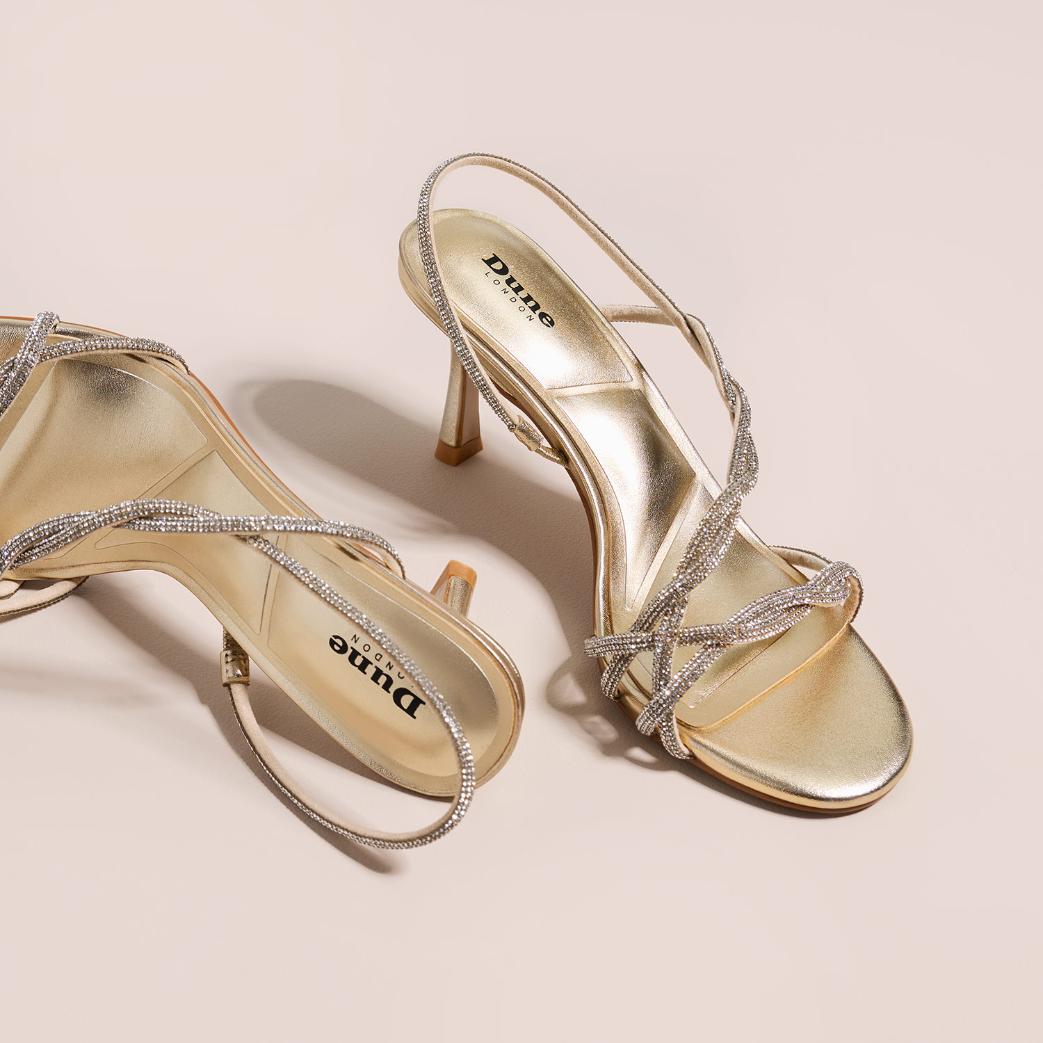 Gold open-toe high heels with rhinestone straps on a beige background.