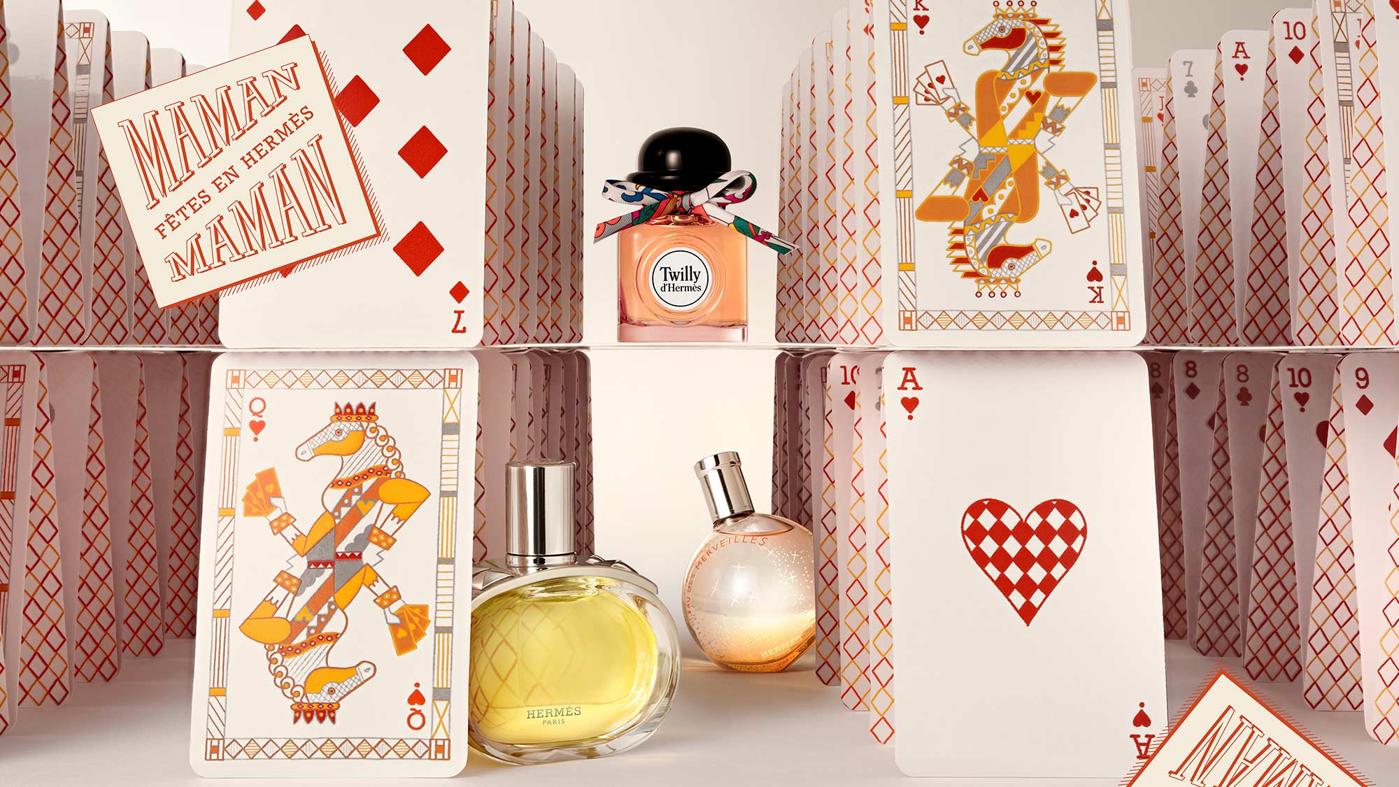 Perfume bottles displayed among a house of playing cards with red and orange designs.