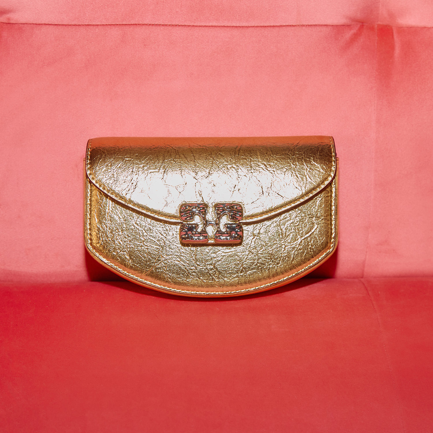 A gold clutch purse with a clasp sits on a red velvet surface.