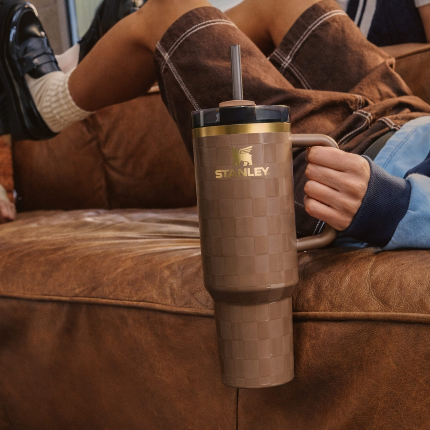 Person holding a large brown travel mug with a straw, sitting on a sofa.