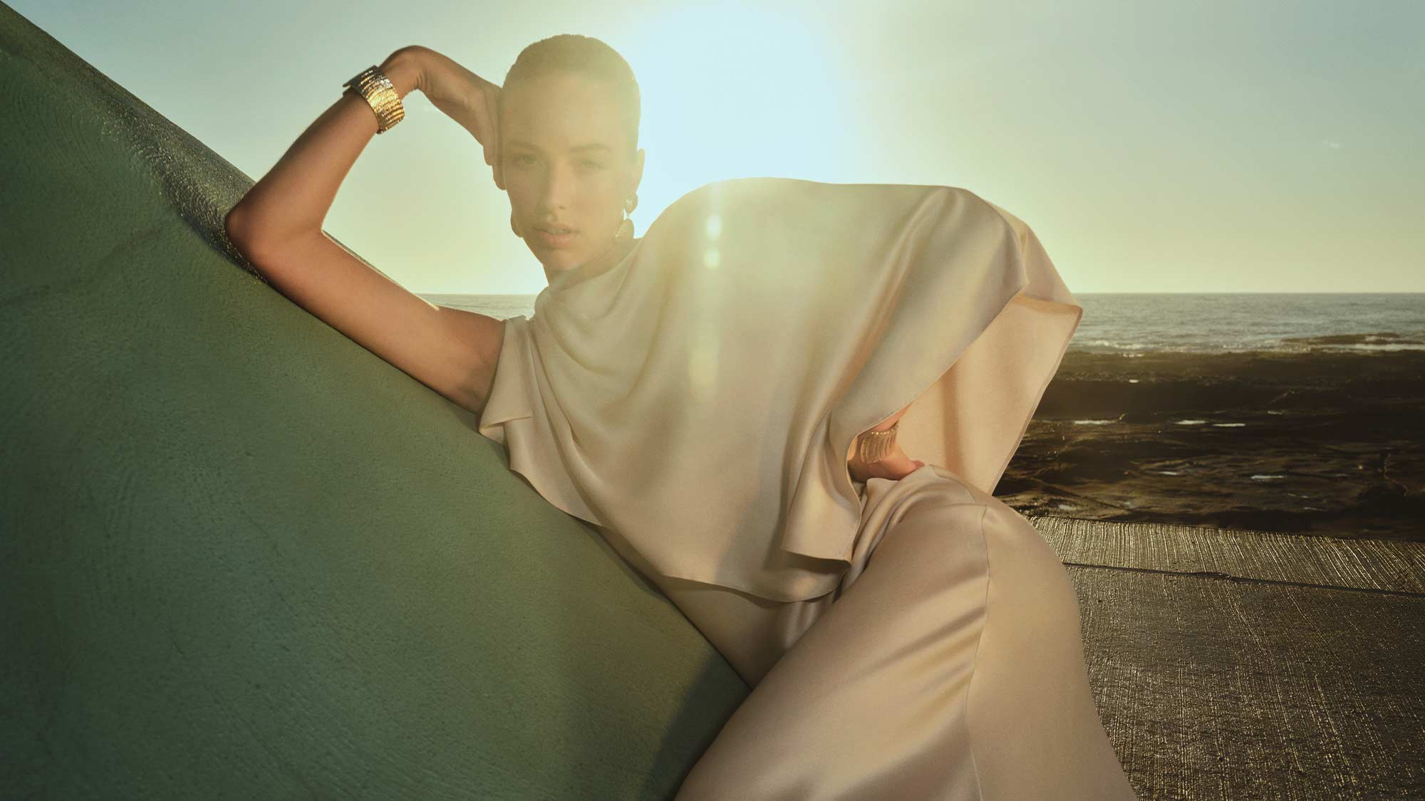 Woman in an elegant, cream cape dress, posing against a wall.