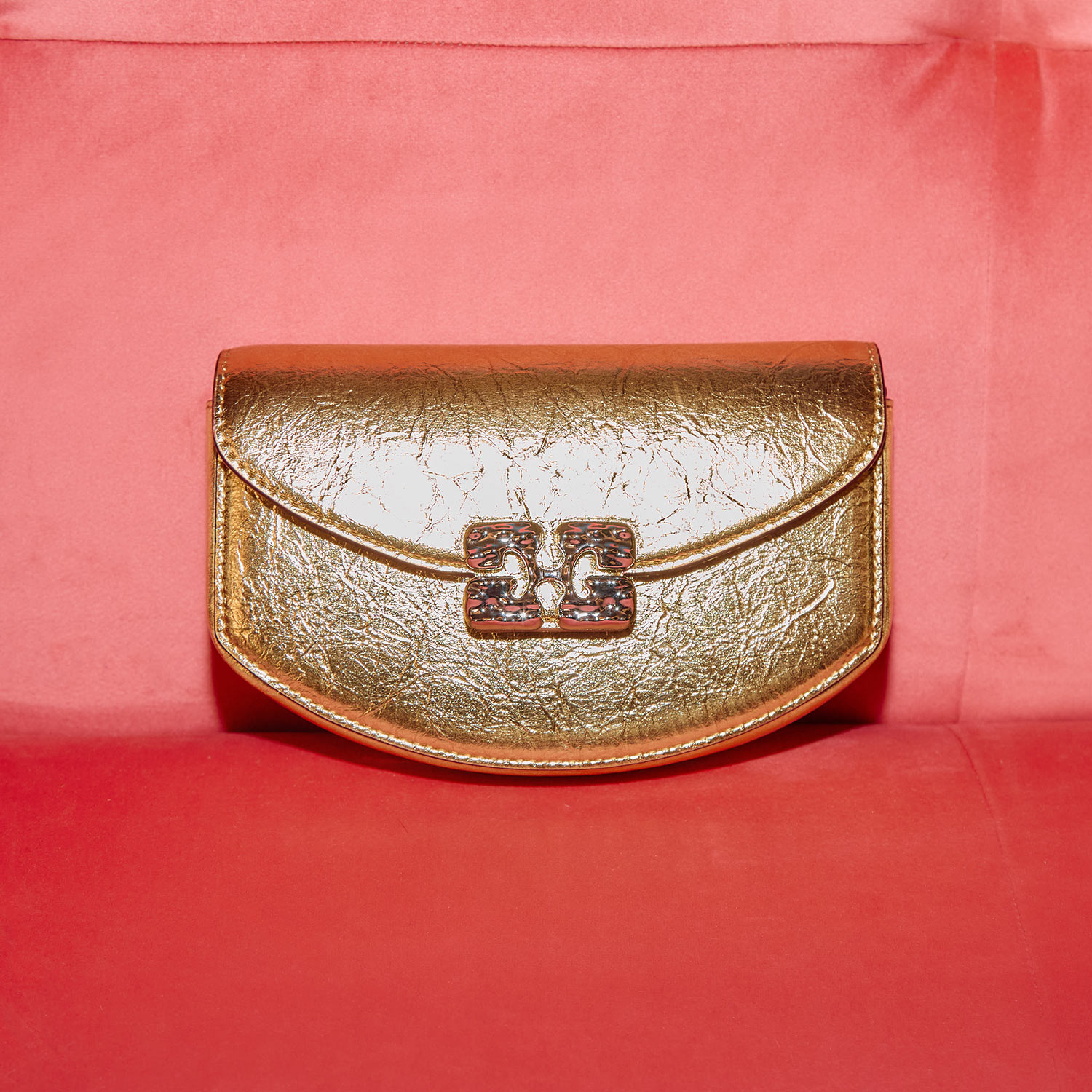 A gold textured clutch with a decorative clasp, set against a red background.