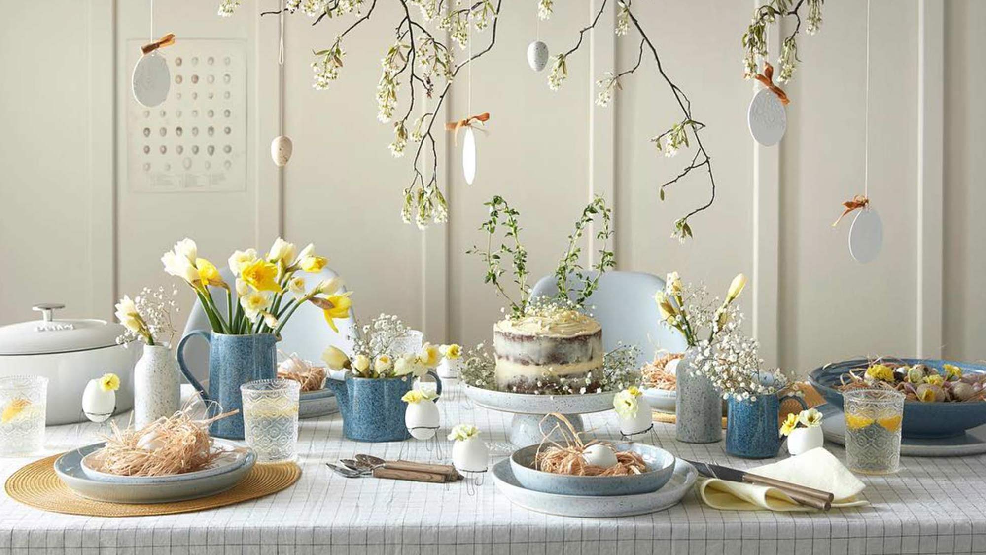 Elegant spring-themed table setting with flowers, a layered cake, and hanging decorations.