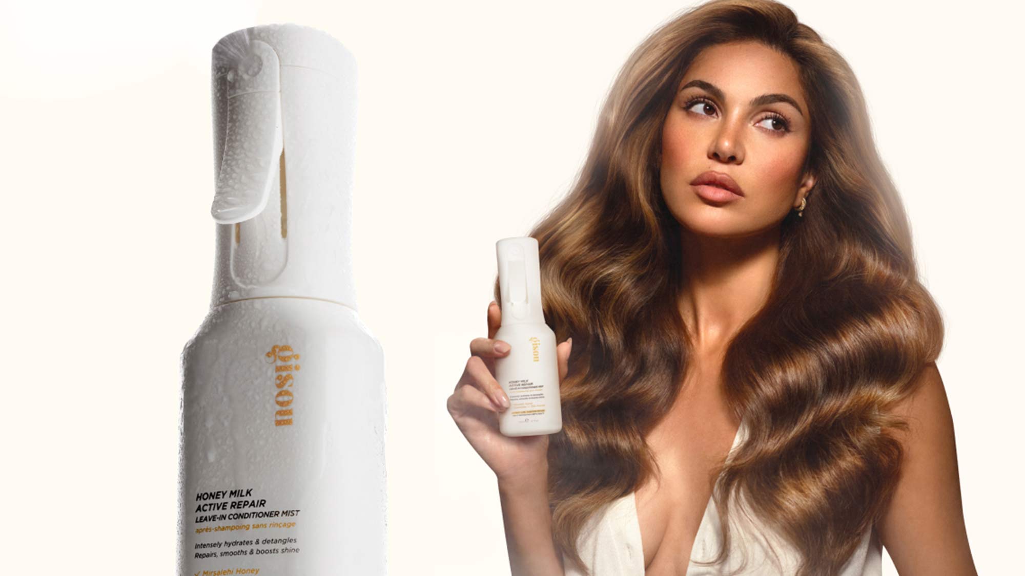 A woman with voluminous hair holds a spray bottle of hair product by IGK.