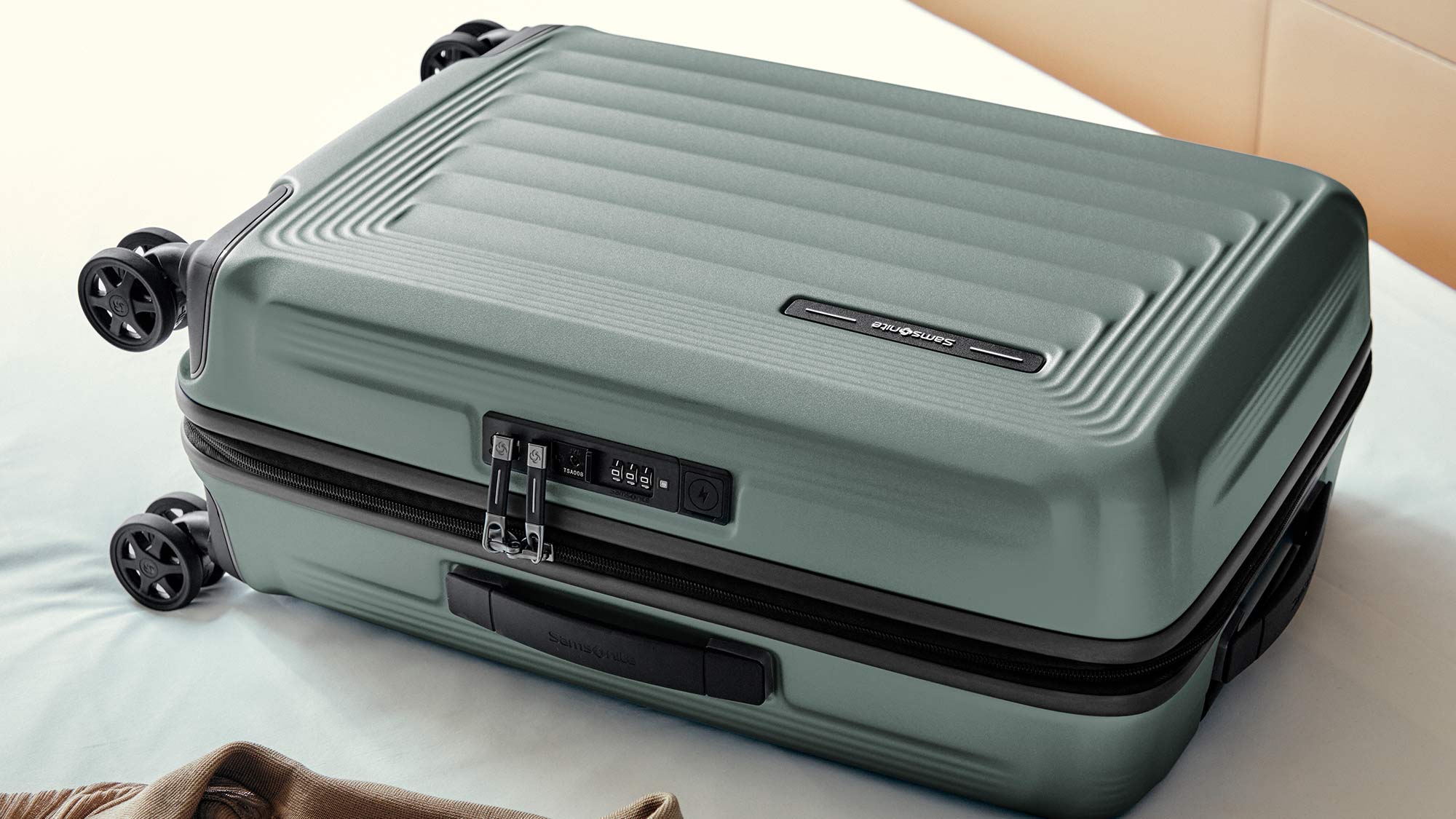 A green hard-shell suitcase with four wheels and a built-in combination lock on a bed.