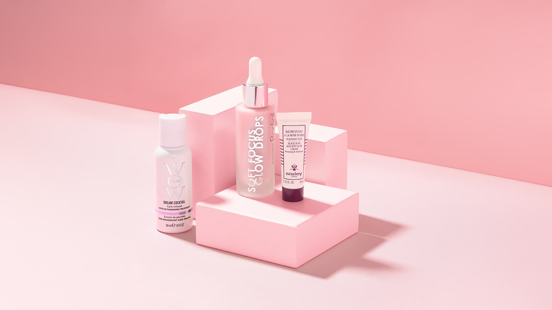 Three skincare products on pink geometric pedestals against a pink background.