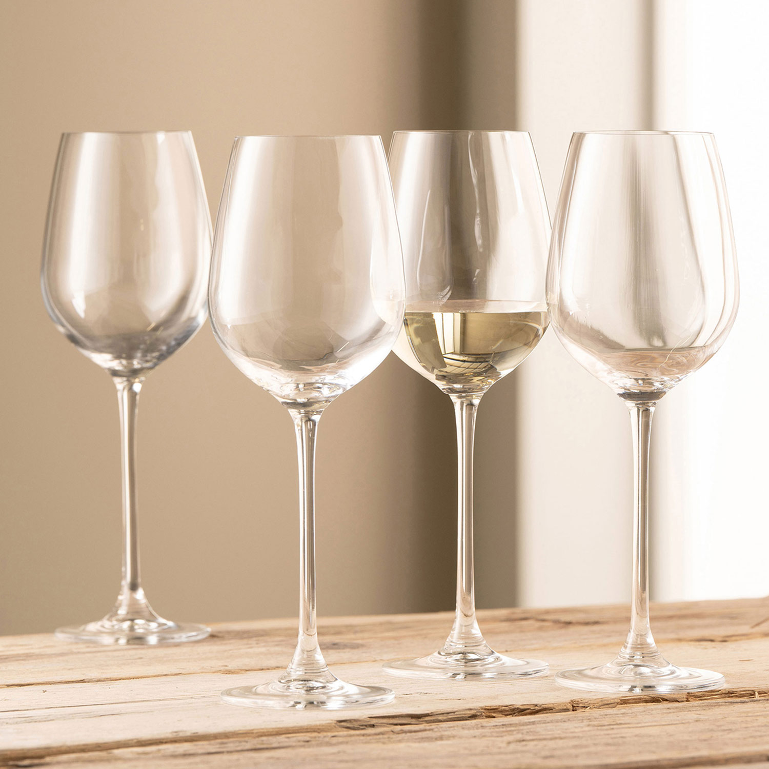 Four empty wine glasses and one partially filled, arranged on a wooden surface.