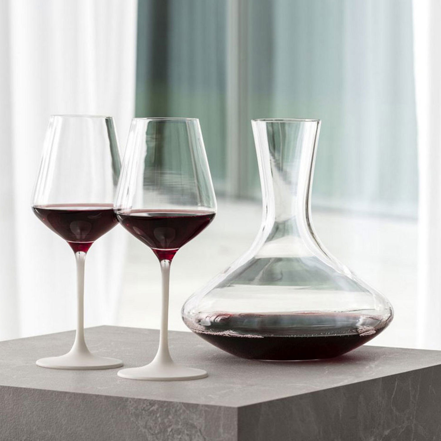 Two glasses and a decanter of red wine on a marble surface, with a bright background.