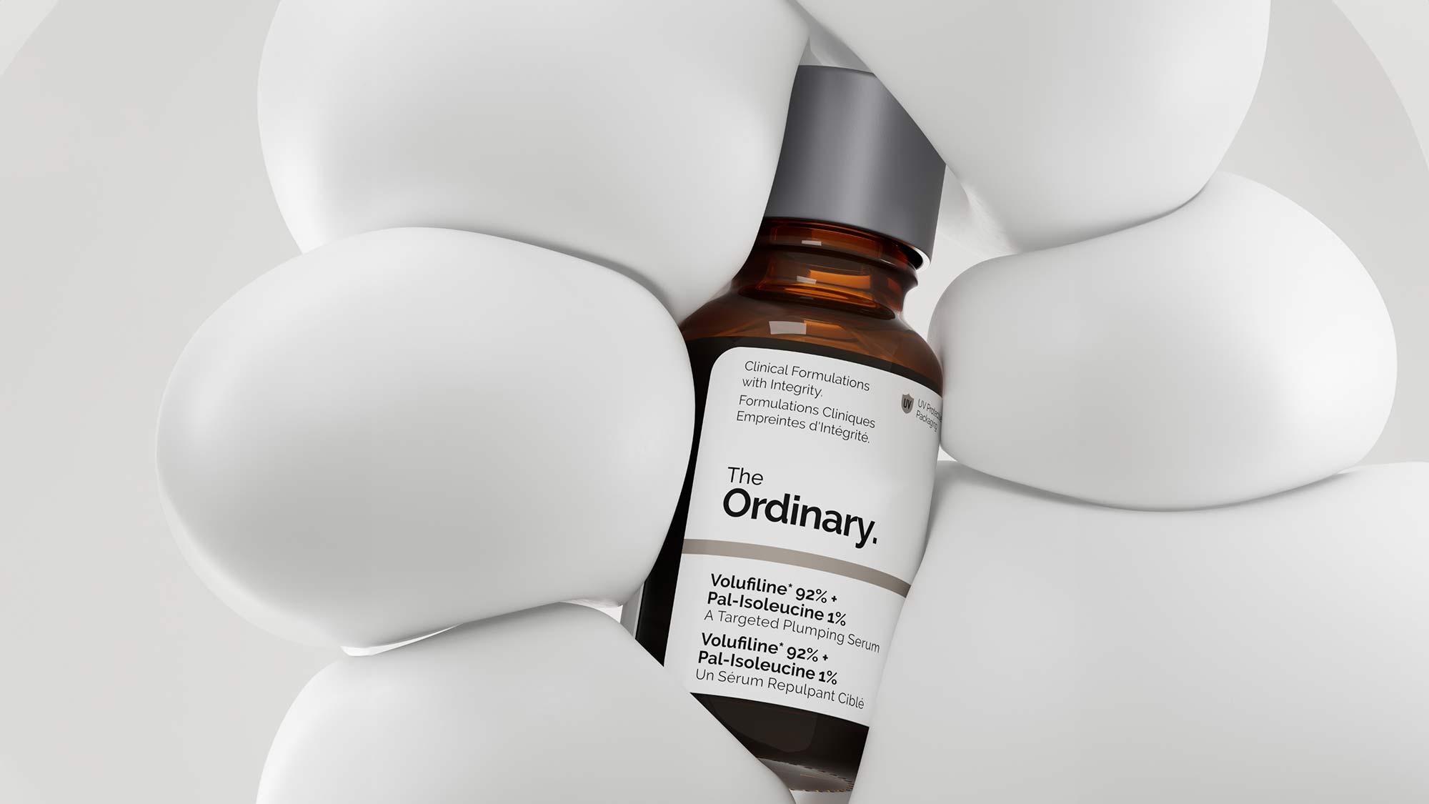A brown bottle of The Ordinary serum is surrounded by abstract white shapes.