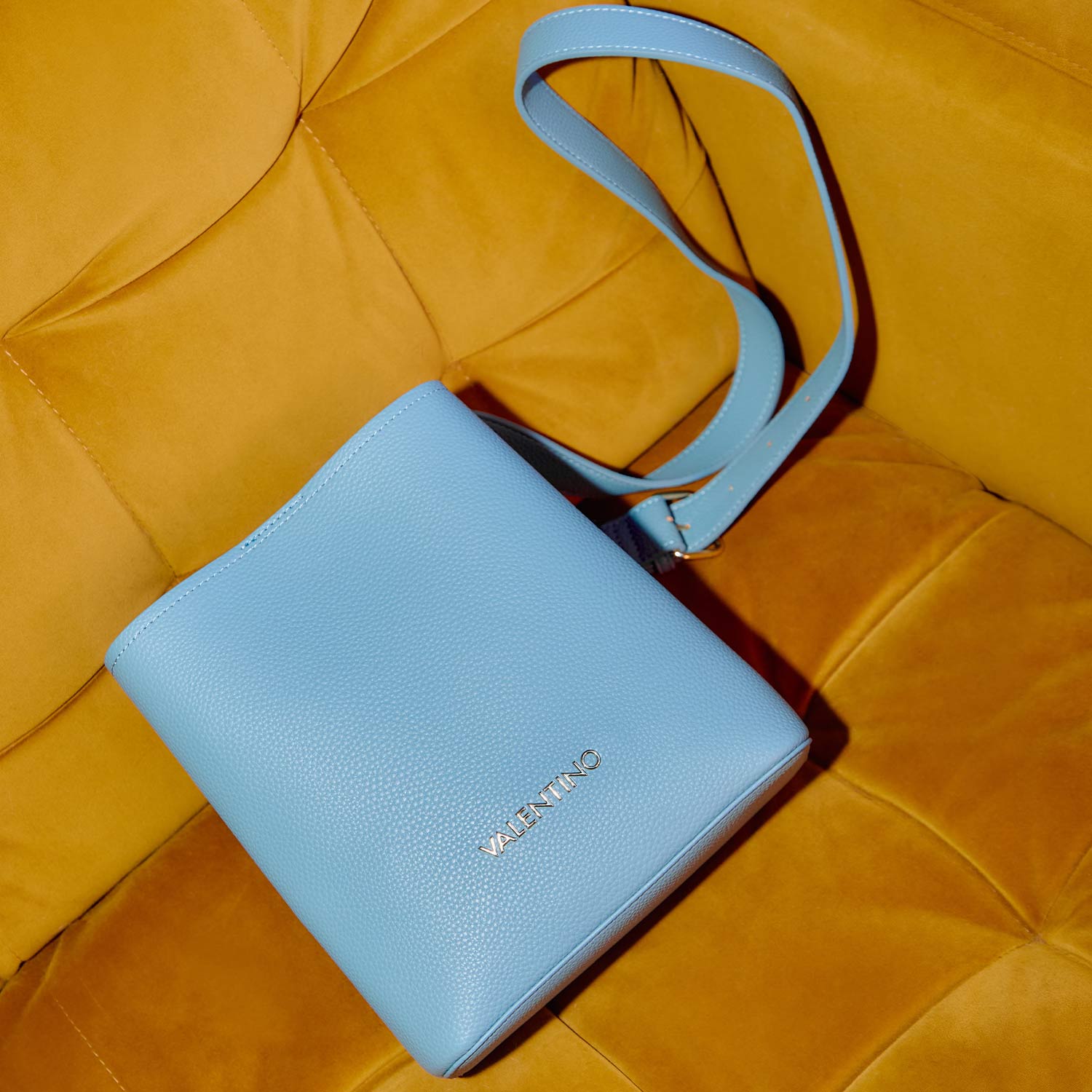 Light blue leather shoulder bag with gold branding on yellow quilted fabric background