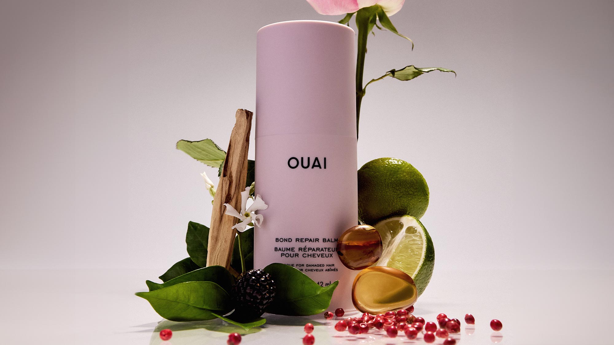 Pink Ouai Bond Repair Balm bottle surrounded by botanicals, lime slices and berries