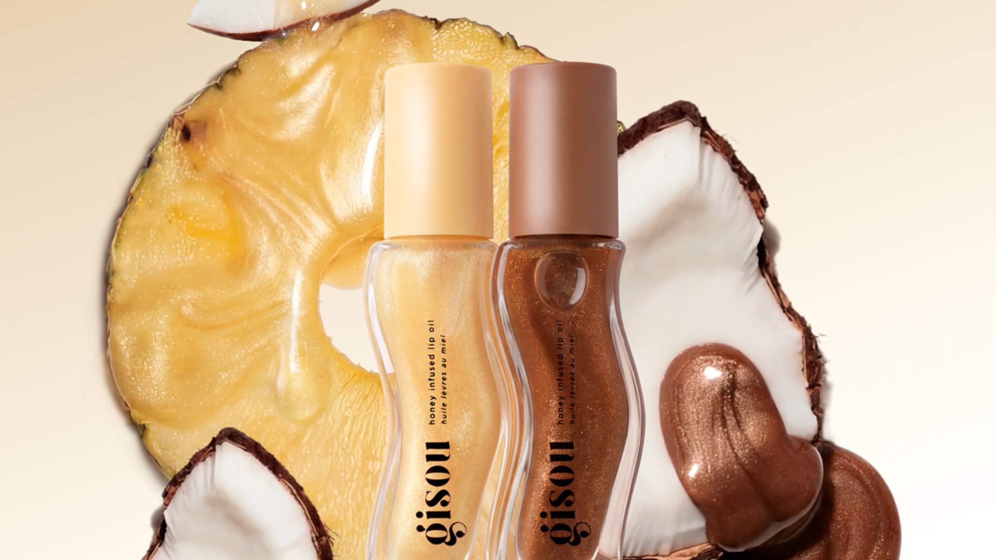 Two bottles of Gisou hair oil are placed against slices of pineapple and coconut.