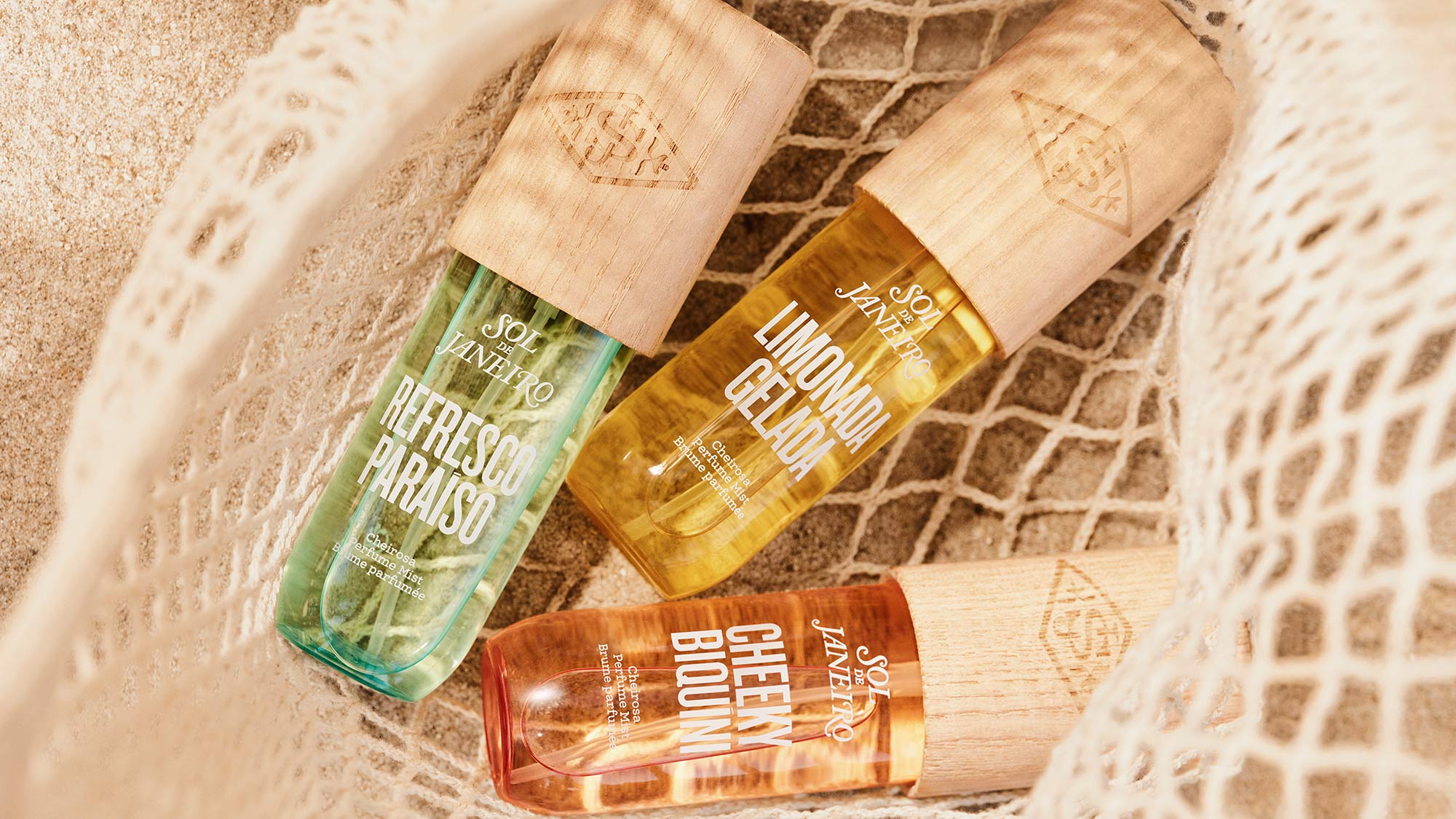 Three Sol de Janeiro body care spray bottles with wooden caps on sandy brick background