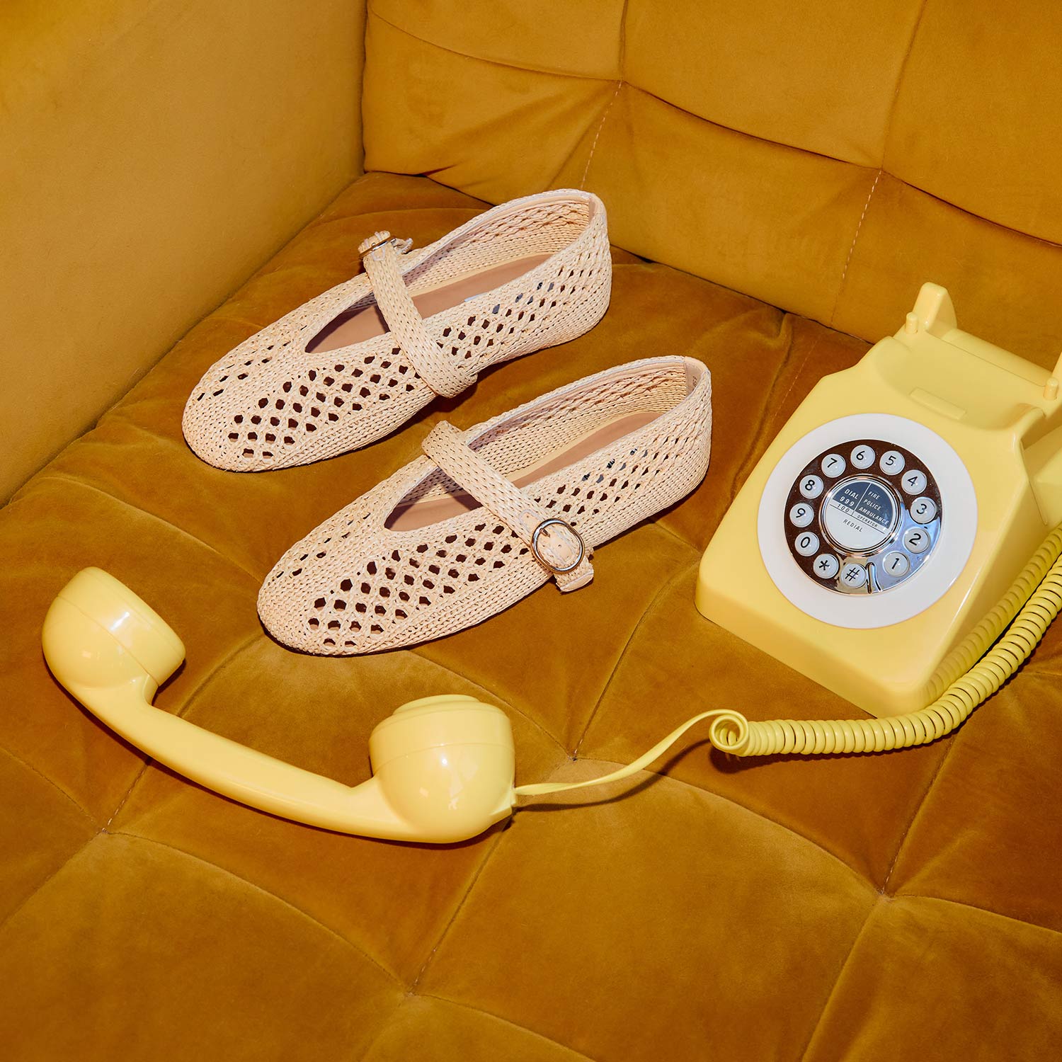 Crochet shoes and a vintage yellow rotary phone on a mustard sofa.