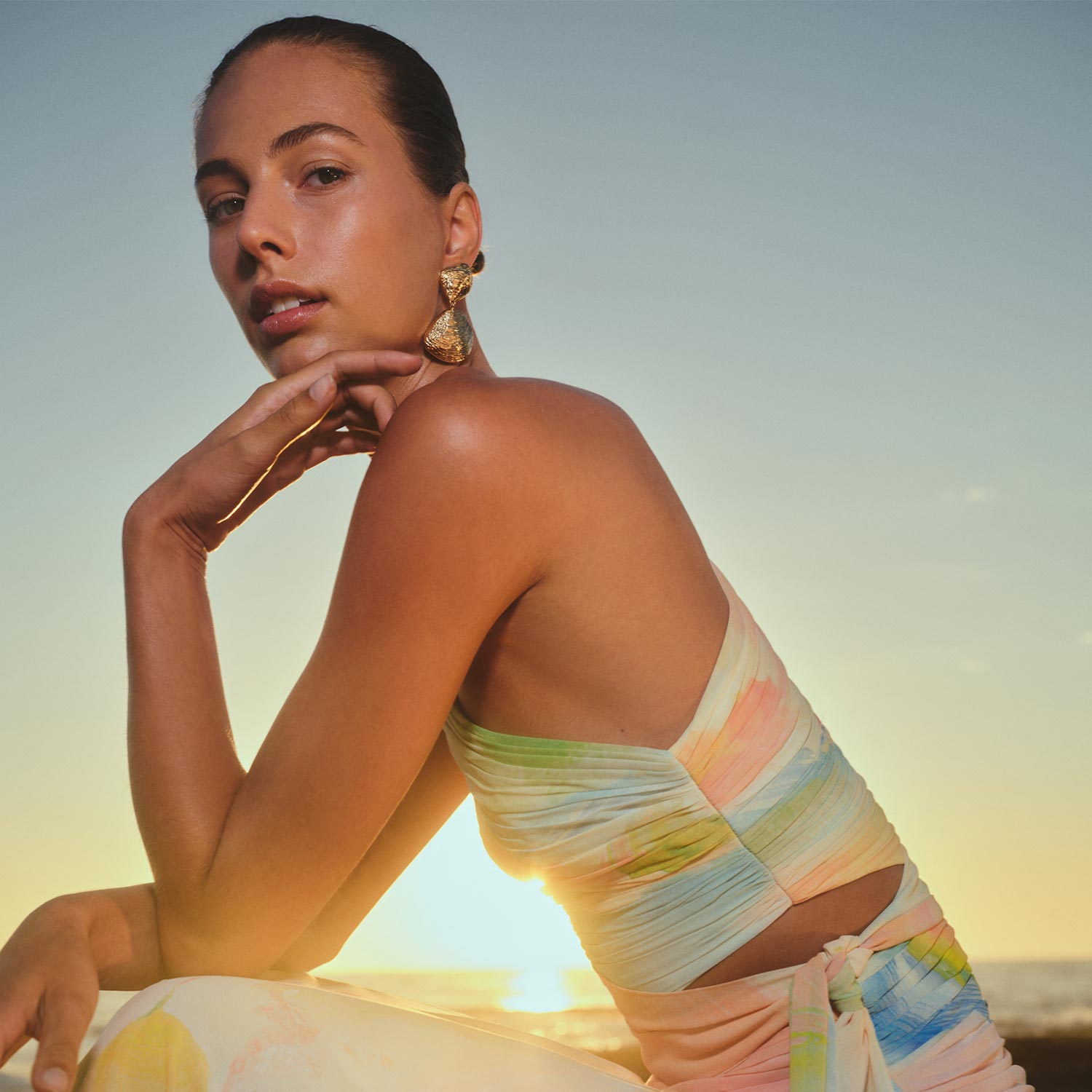 Woman wearing gold drop earrings and light-coloured wrap against blue sky background
