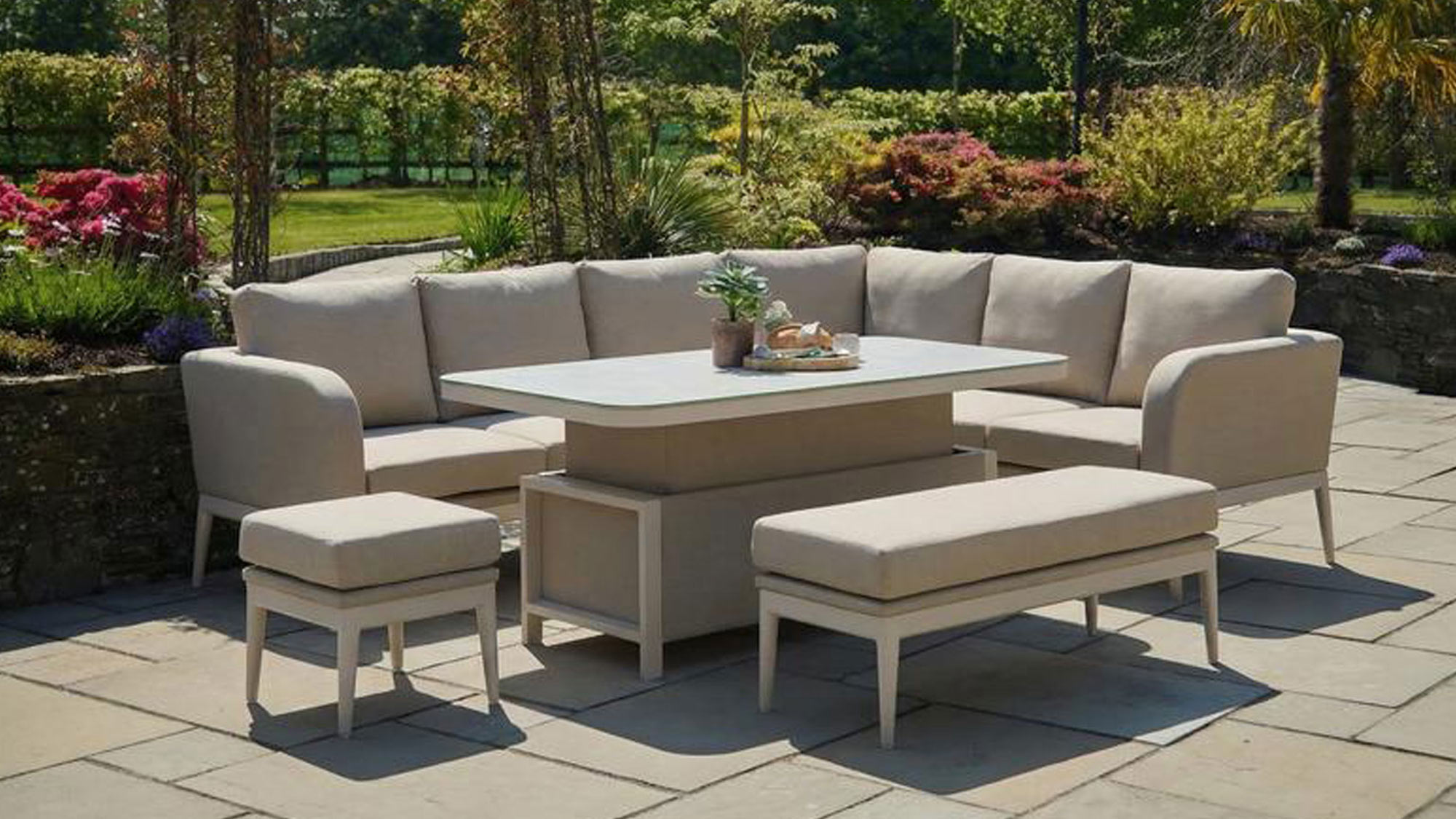 Cream garden furniture set with corner sofa, dining table and benches on patio overlooking landscaped garden