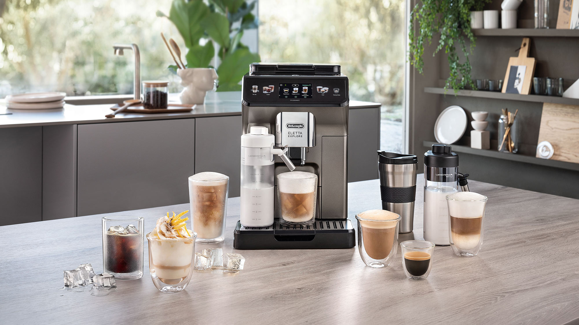 DeLonghi black automatic coffee machine surrounded by various specialty coffee drinks and accessories on wooden kitchen counter