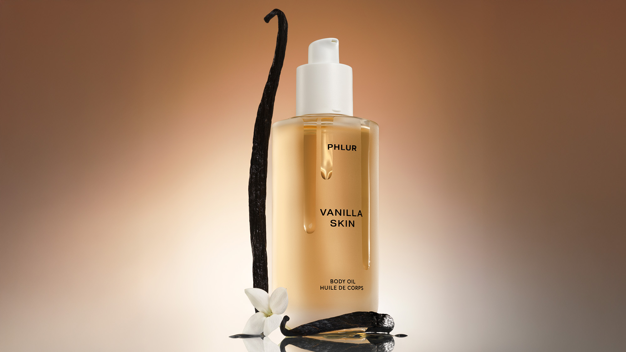 A bottle of vanilla-scented body oil with a vanilla pod and flower beside it.