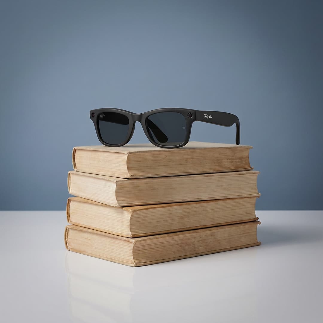 A stack of five vintage books rests on a white surface against a blue background. A pair of black sunglasses is placed on top of the books.