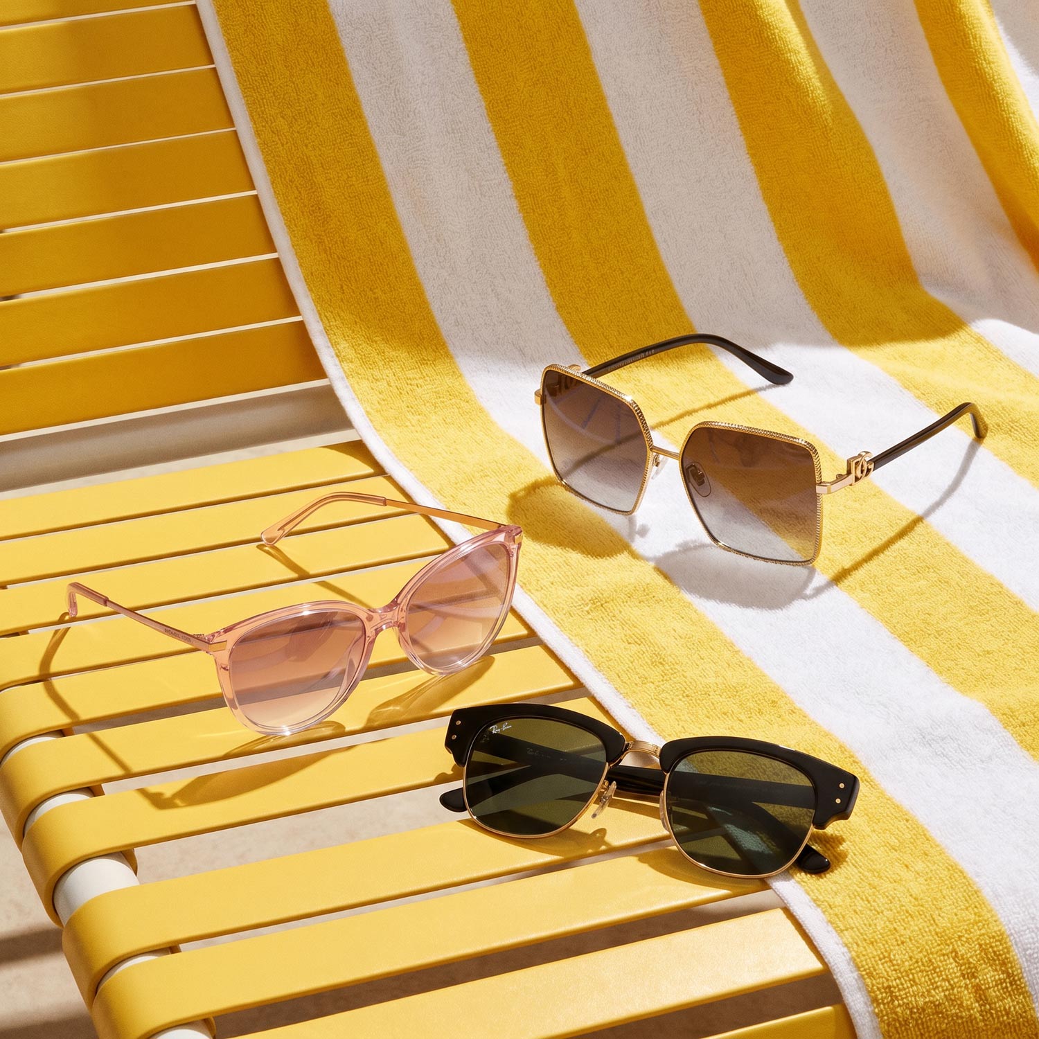 Three stylish sunglasses displayed on a yellow and white striped deck chair in bright sunlight