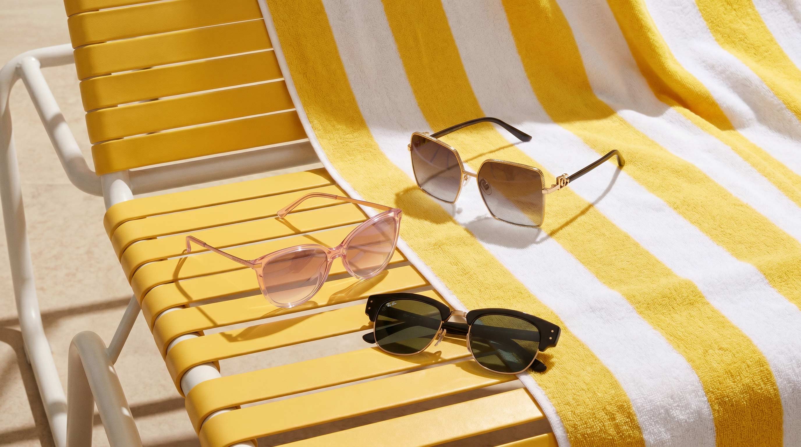 Three stylish sunglasses displayed on a yellow and white striped deck chair in bright sunlight