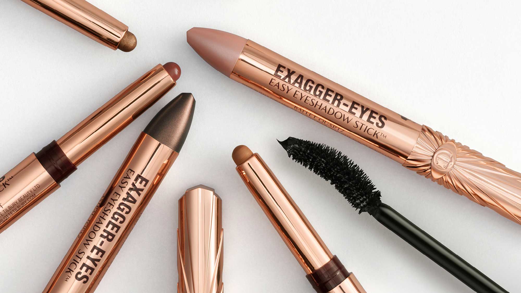 Charlotte Tilbury Exagger-Eyes eyeshadow sticks and mascara in rose gold packaging displayed with swatches.