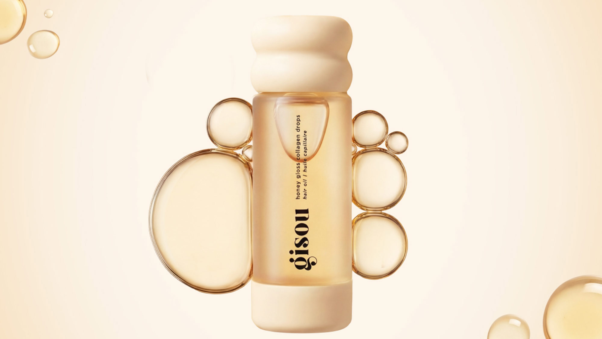 Gisou Honey Gloss Collagen Drops hair serum bottle surrounded by water droplets on cream background.