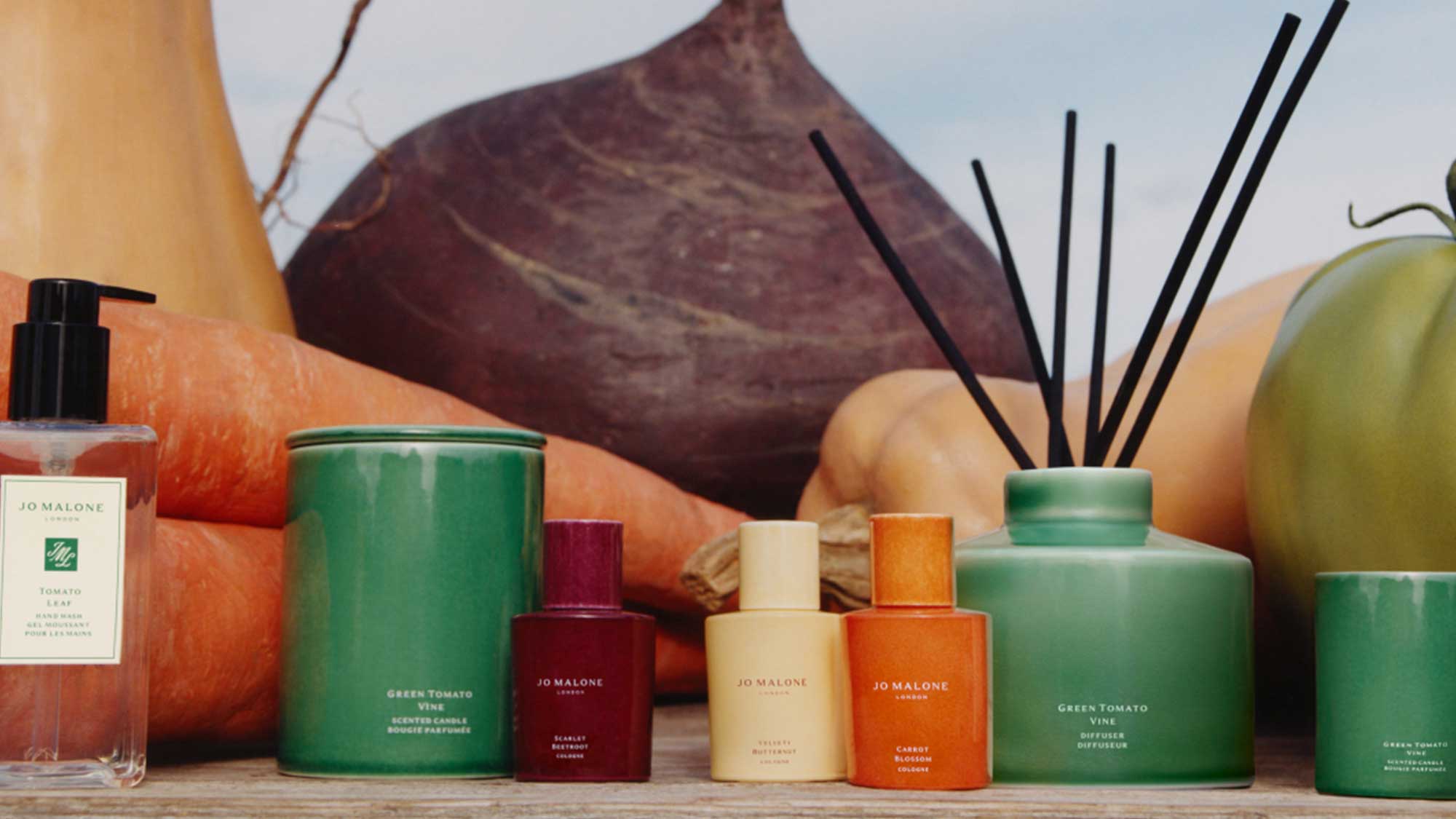 Jo Malone London fragrance collection with harvest-inspired bottles, candles, and diffuser surrounded by vegetables.