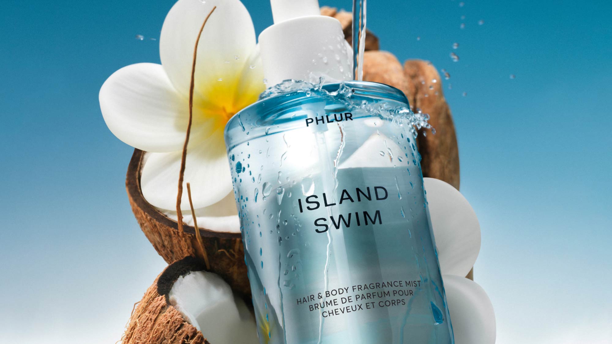 Phlur Island Swim hair and body fragrance mist bottle with water droplets, surrounded by white flowers and coconut on blue background